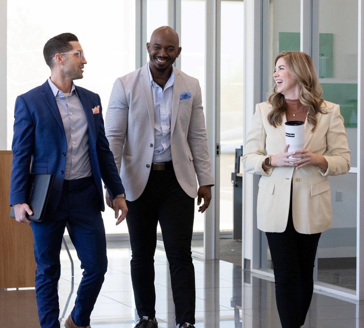 Two male and one female team member talk and laugh while walking through a lobby