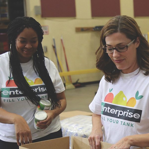 Two women and one man packing food in Fill Your Tank boxes