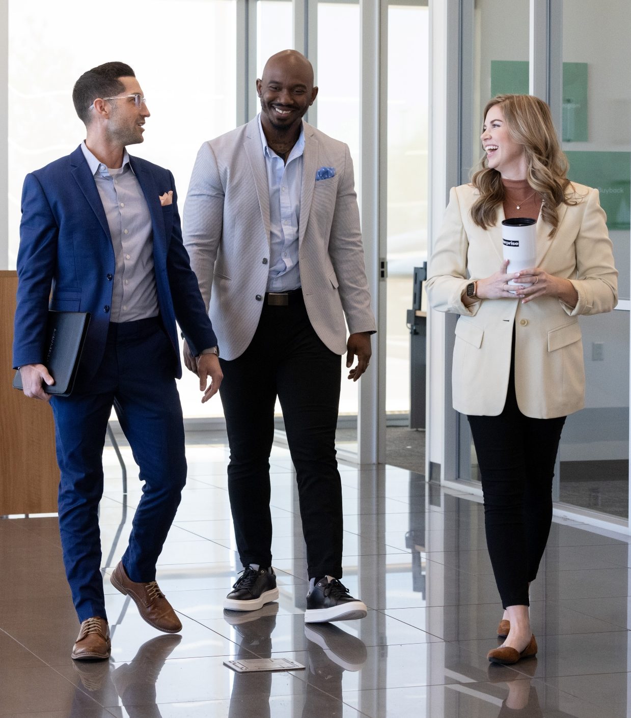 Two male and one female team member talk and laugh while walking through a lobby