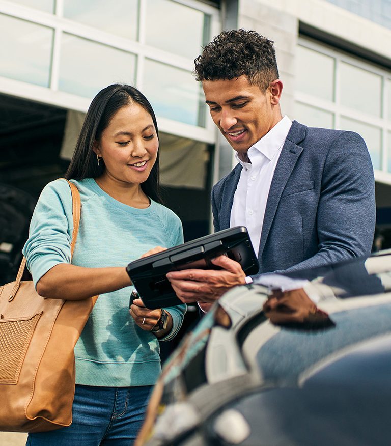 A woman and man look over an iPad at a car lot