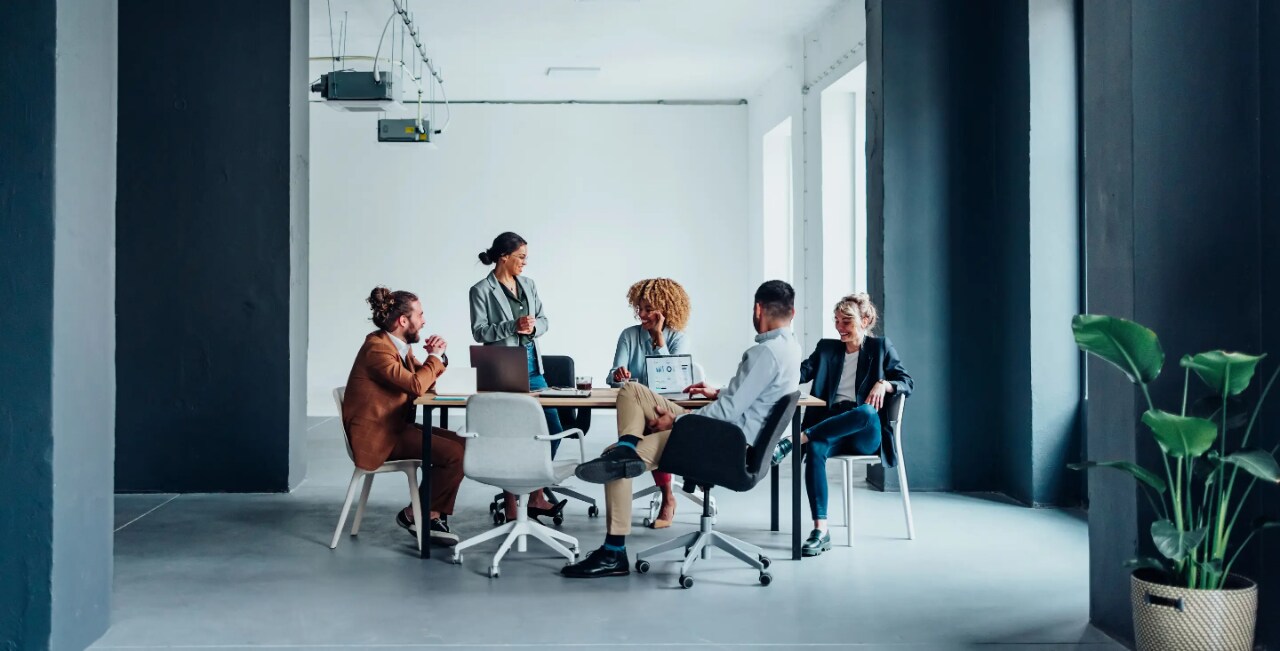 A woman addresses a group of colleagues seated around a conference table.