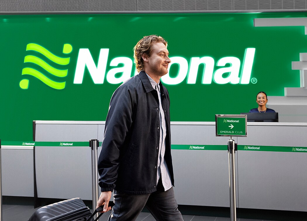 A male customer walks through an airport lobby as a female employee from the National Car Rental desk looks on