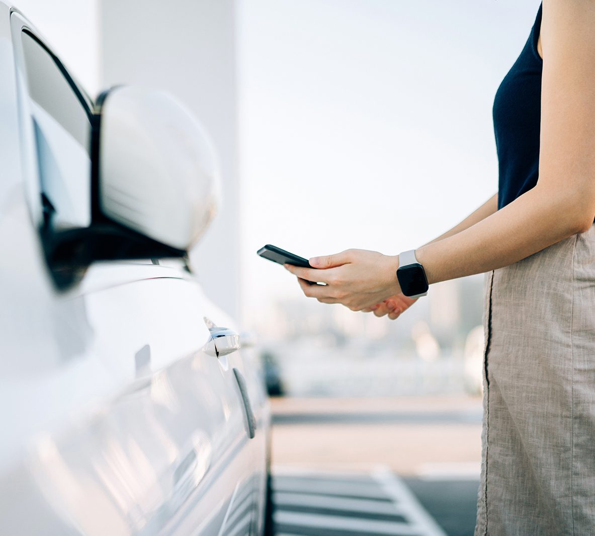 Woman holding phone up against white vehicle.