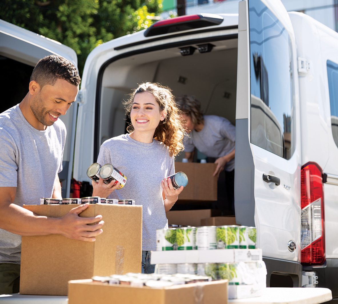 Light-skinned male and white female hold canned goods on the backside of a truck.