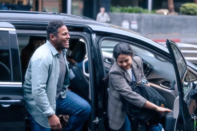 Two smiling men, one getting out of the passenger seat of a van, the other getting out of the middle row.
