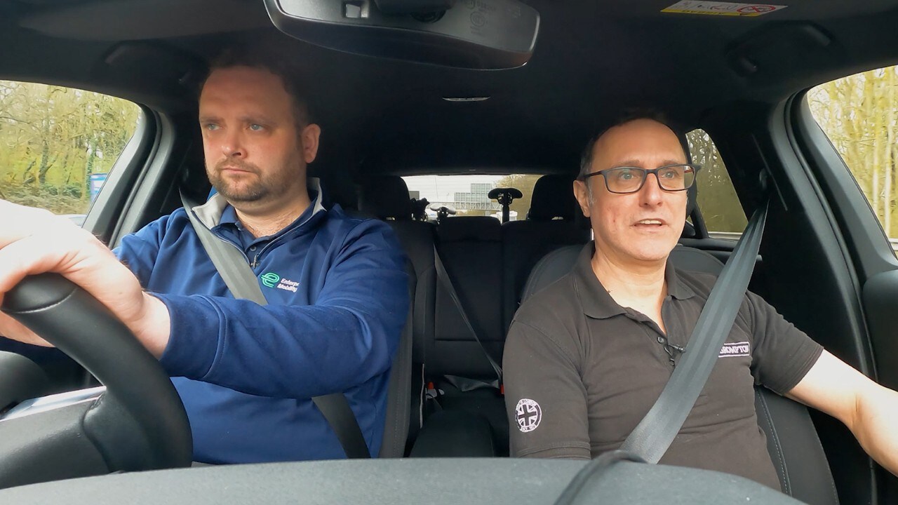 A white car drives on the road with green grass all around