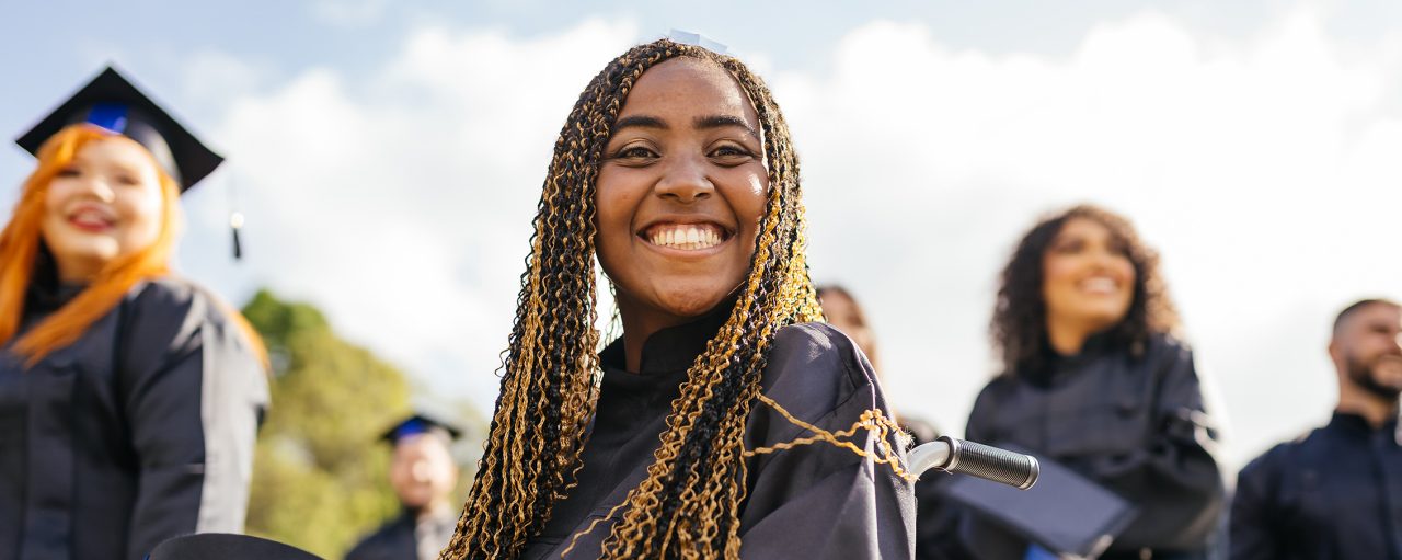 A female with long braided hair smiles at her college graduation ceremony